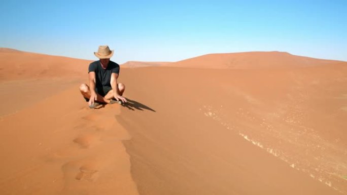WS男性游客在非洲纳米比亚的沙漠沙丘上sc取锈色的沙子