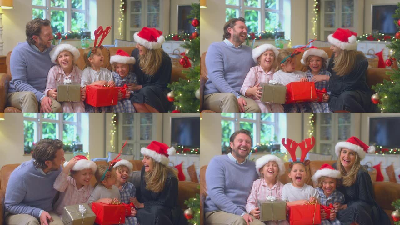 戴着圣诞老人帽子的家庭坐在家里的沙发上打开圣诞礼物