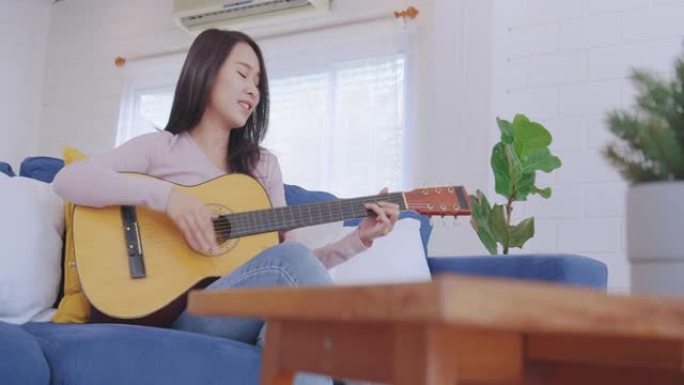 迷人的亚洲年轻成年女性喜欢在客厅弹吉他和唱歌