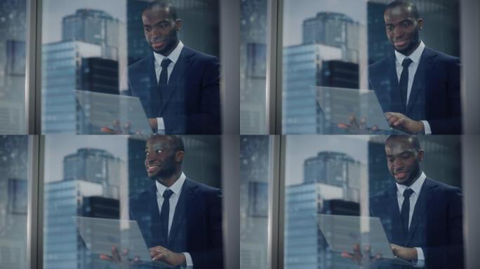 成功的黑人商人的肖像穿着西装站着，用笔记本电脑看着办公室窗外。微笑股市投资经理与电脑合作从外面拍摄