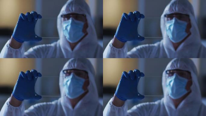 在实验室中使用手持接口穿着防护服和手套的白人男性医务人员