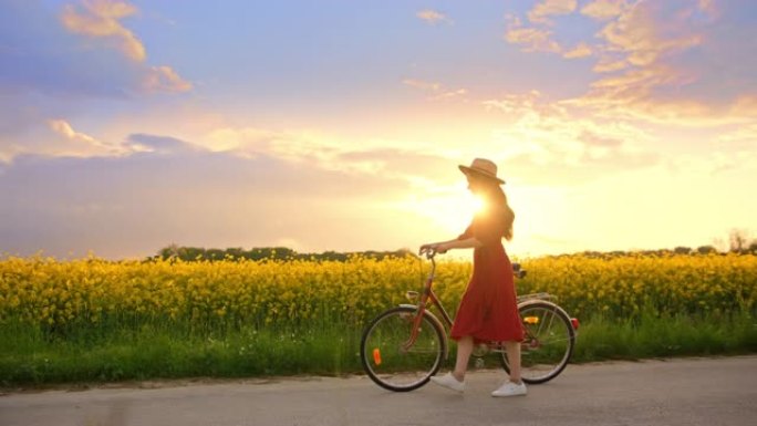 跟踪拍摄一个穿着红色连衣裙戴着帽子的黑发女人的照片，她骑着自行车被金鱼草的花朵包围着，背景是日落，慢
