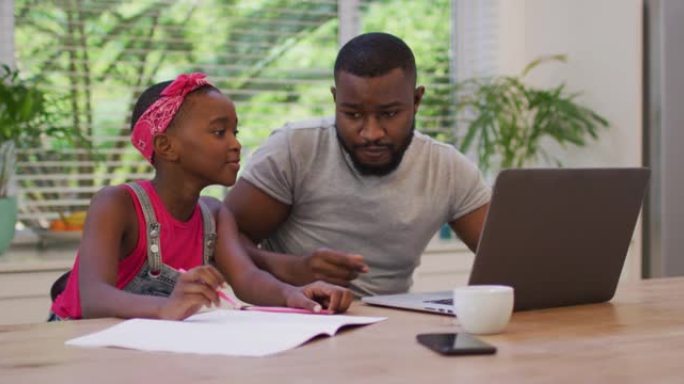 非裔美国父亲使用笔记本电脑并在家里帮助女儿做作业