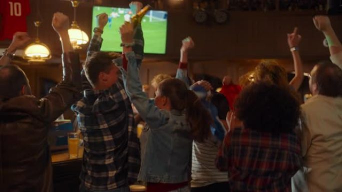 一群足球迷在体育酒吧观看现场足球比赛。人们站在电视机前，为他们的团队欢呼。球员进球，人群庆祝赢得冠军