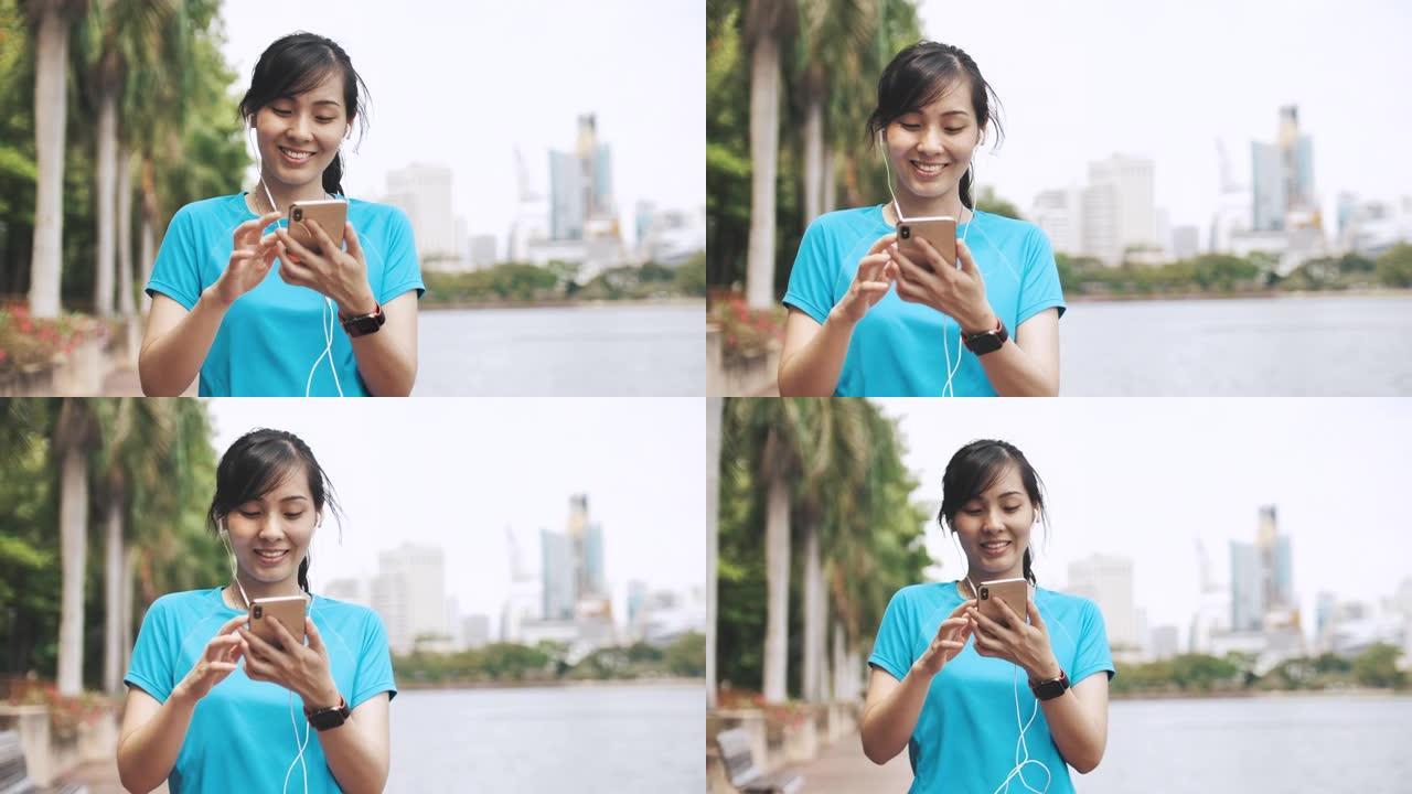 微笑的运动女人正在使用智能手机在城市中行走