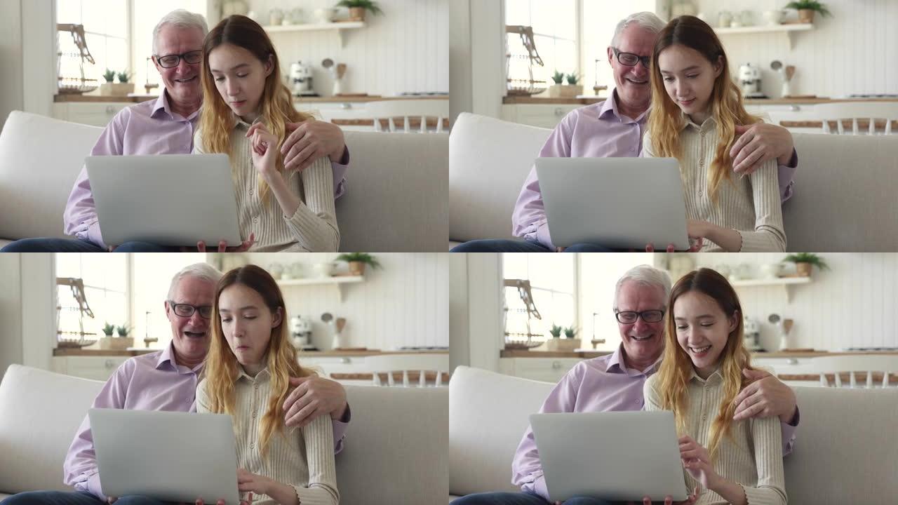 年长的爷爷和十几岁的孙女花时间使用现代笔记本电脑