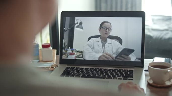 男子病人在家中使用笔记本电脑与亚洲女医生交谈