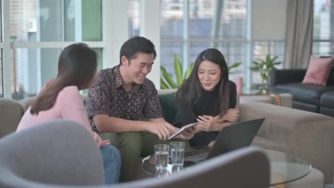 亚洲华人朋友同事坐在大堂休息室的沙发上，与笔记本电脑保持联系