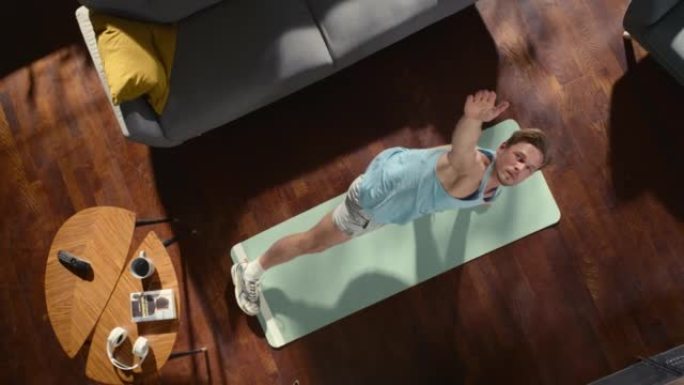 顶视图运动: 漂亮的家伙在家里的运动垫上做瑜伽伸展。肌肉发达，健康，英俊的运动员在他的公寓里做健身锻