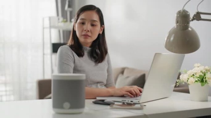 坐在办公桌前的女人在笔记本电脑上工作，在带有AI辅助功能的智能扬声器旁边回答问题