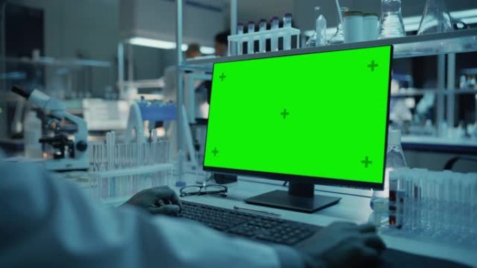 在应用科学研究实验室中，在带有绿屏模拟模板的台式计算机上工作的医学研究科学家。白大褂的实验室工程师在