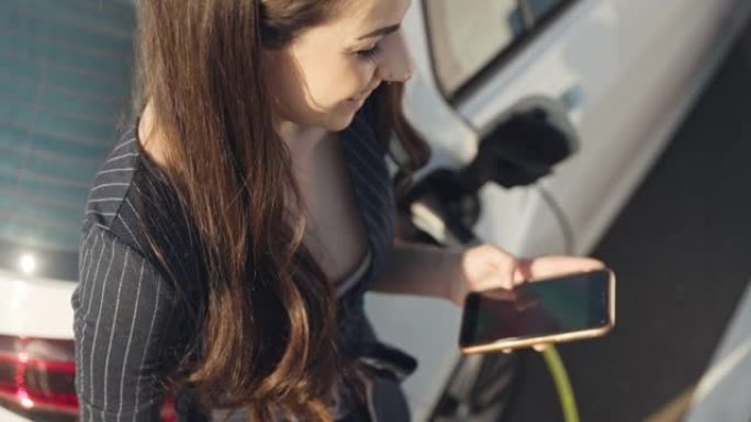年轻女子在给电动汽车充电时使用手机