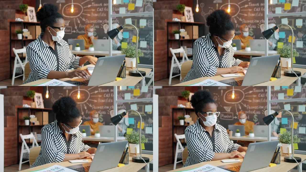 非裔美国女商人戴着医用口罩，使用笔记本电脑在办公室工作