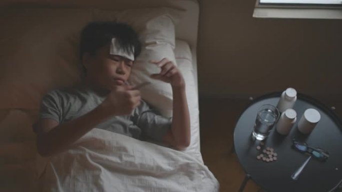 亚洲中国病童躺在床上，嘴里含着温度计测量体温
