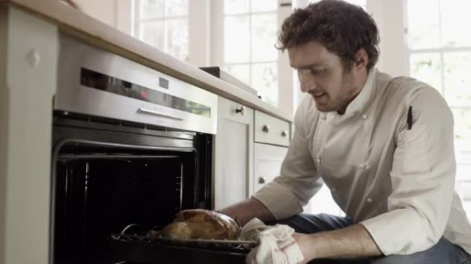 一位年轻厨师从家里的烤箱里拿出一只鸡的镜头