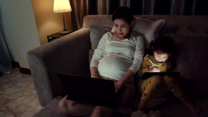 迷人的怀孕母亲工作，而女儿晚上使用数字平板电脑。