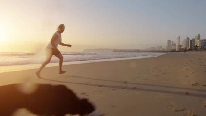 4k视频片段，一个女人在日落时与狗在海滩上玩耍