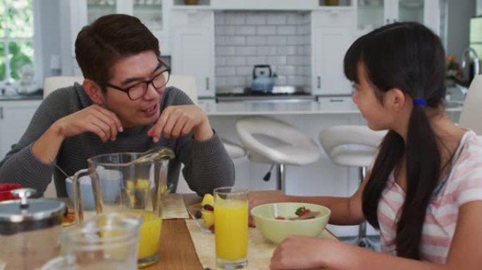 快乐的亚洲父亲在厨房吃早餐和女儿聊天