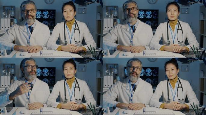 亚洲妇女和白人男子在黑暗办公室的医疗网络研讨会上说话和看着相机