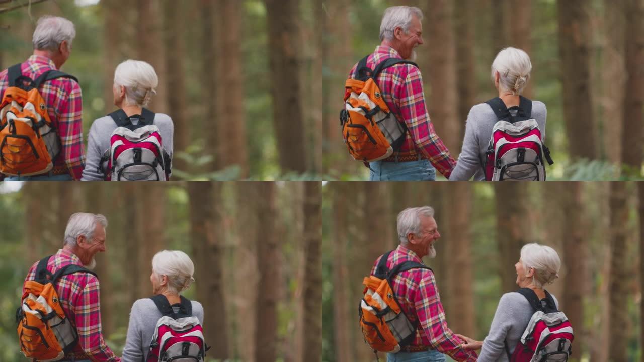 微笑活跃的老年夫妇手牵手一起徒步穿越林地乡村的后视镜头 -- 慢动作拍摄