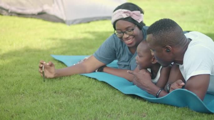 SLO MO快乐的父母，他们的女儿躺在公园的肚子上，在智能手机上观看视频