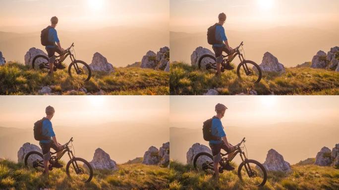 山地自行车骑手站在山的边缘，在日落时欣赏壮丽的景色