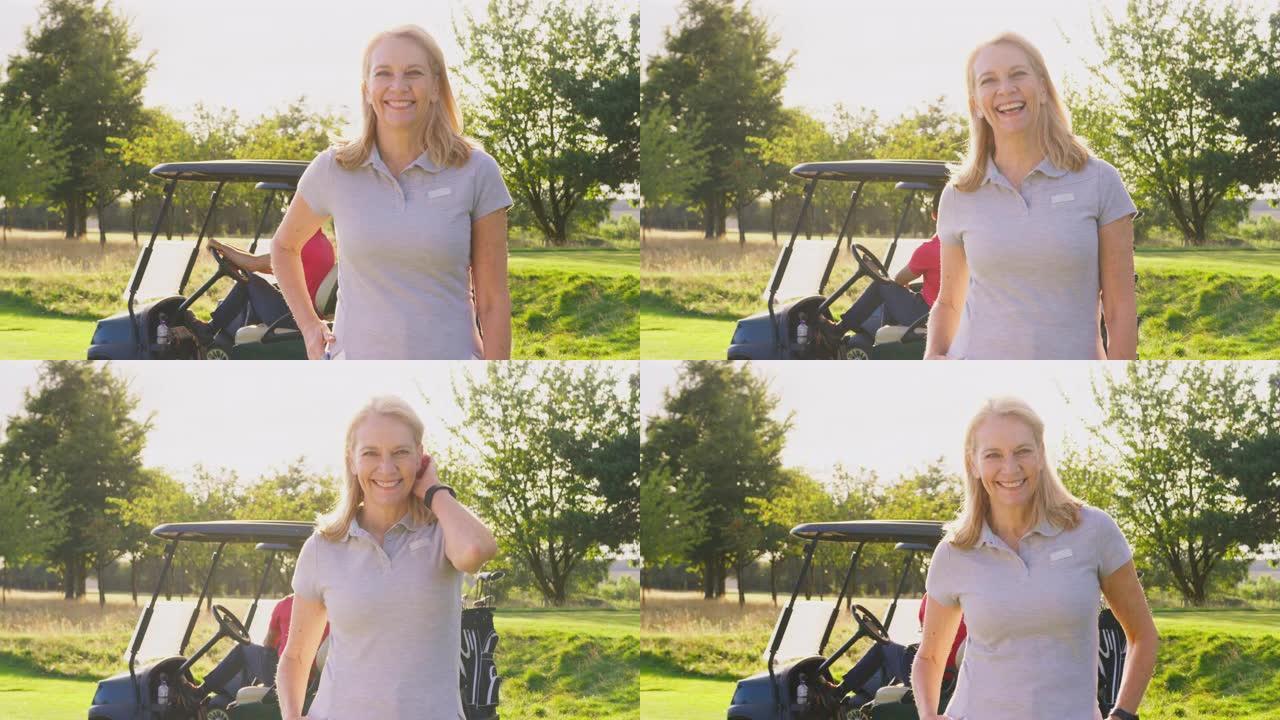 微笑的成熟女高尔夫球手站在高尔夫球场上的童车旁边的肖像