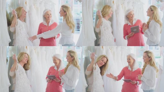销售助理或商店老板用数字平板电脑帮助母亲和成年女儿在新娘商店选择婚纱-慢动作拍摄