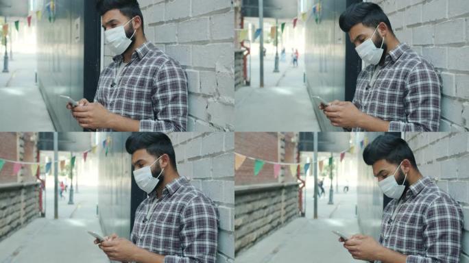 在城市户外使用智能手机发短信的阿拉伯年轻人戴着医用口罩的慢动作