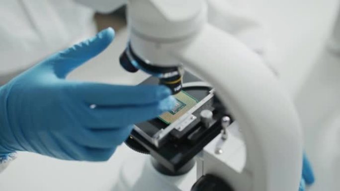 穿着工作服和手套的工程师/科学家的特写镜头使用显微镜检查主板微处理器组件