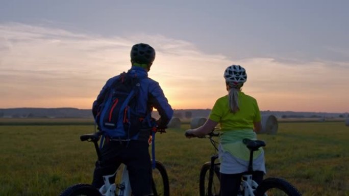 SLO MO夫妇骑自行车的人在草地上欣赏日落时互相击掌