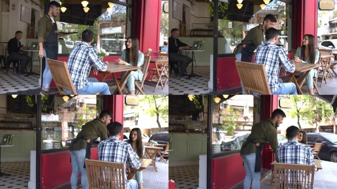拉丁美洲服务员为坐在咖啡馆外的幸福夫妇提供订单