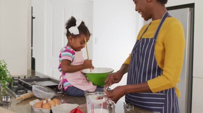 快乐的非洲裔美国母亲和女儿穿着围裙在厨房做饭