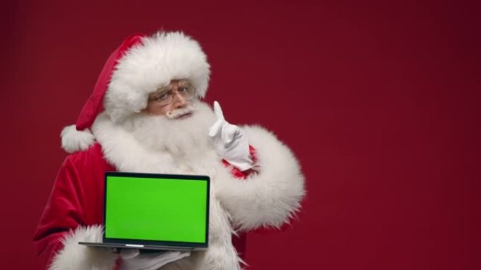 一位困惑的圣诞老人在红色背景下手持笔记本电脑，显示相机中的色度键