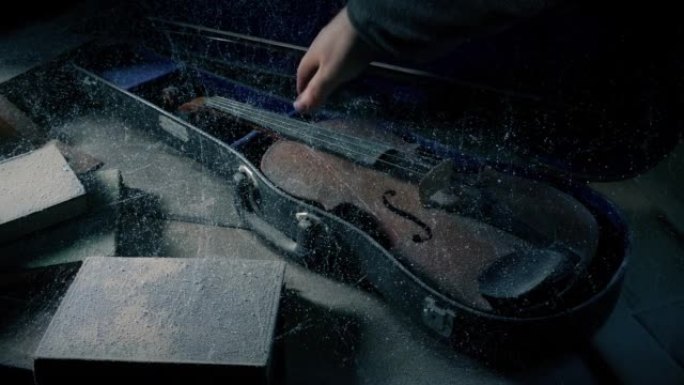 男子从尘土飞扬的桌子上拿起一把旧小提琴