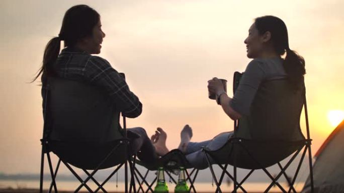 露营日落背景下的两个露营者女人喝彩杯咖啡