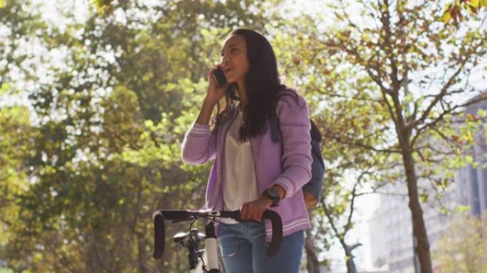 站在公园里，骑着自行车微笑的亚洲妇女在智能手机上聊天