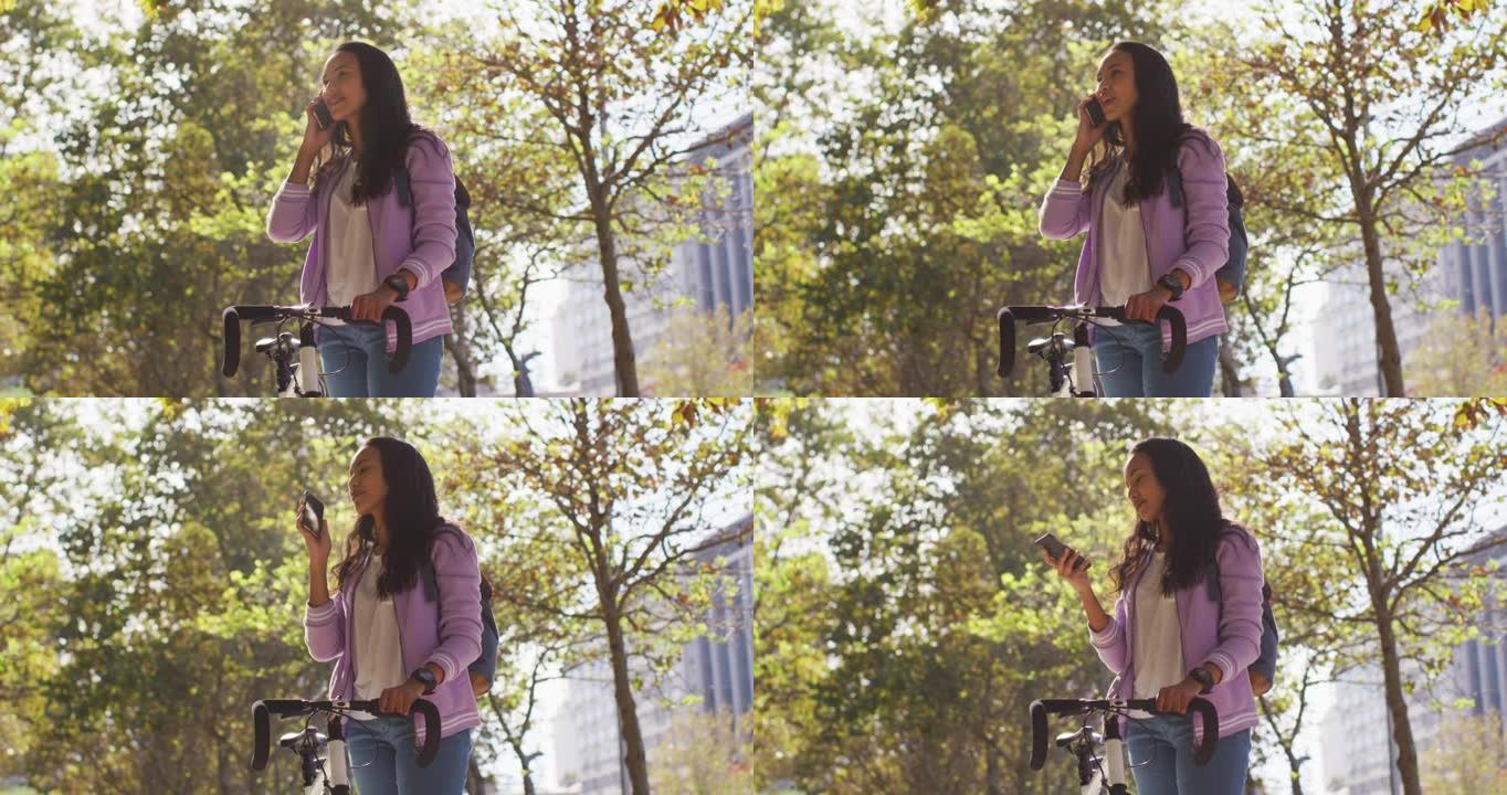 站在公园里，骑着自行车微笑的亚洲妇女在智能手机上聊天