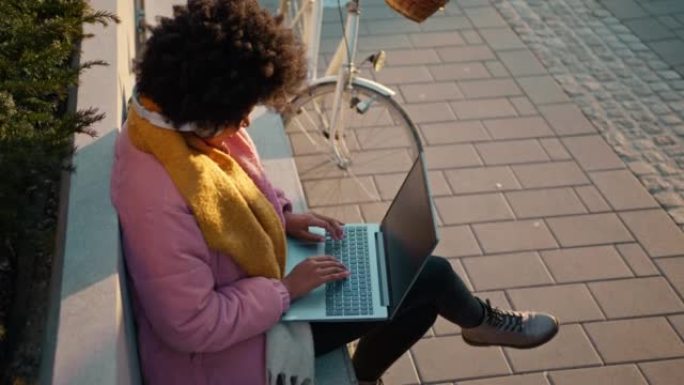 年轻女子坐在城市的长椅上用笔记本电脑工作
