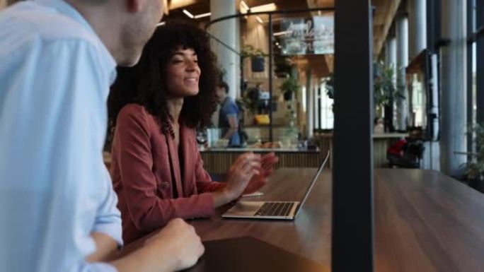 非洲女商人拿着笔记本电脑与坐在咖啡馆的同事讨论工作