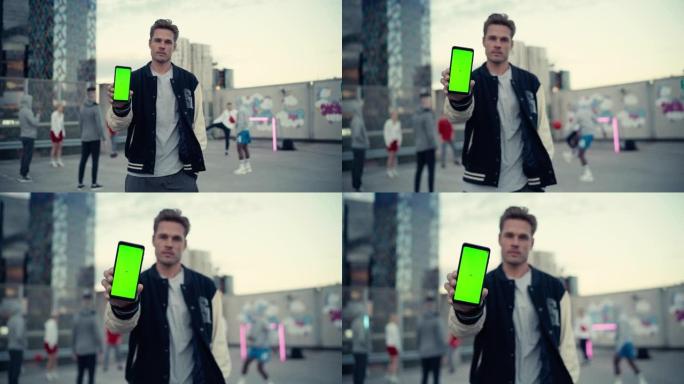 英俊的白人男子拿着智能手机，显示绿屏模拟显示。年轻时尚的男人站在城市环境中，背景中各种各样的人踢街头