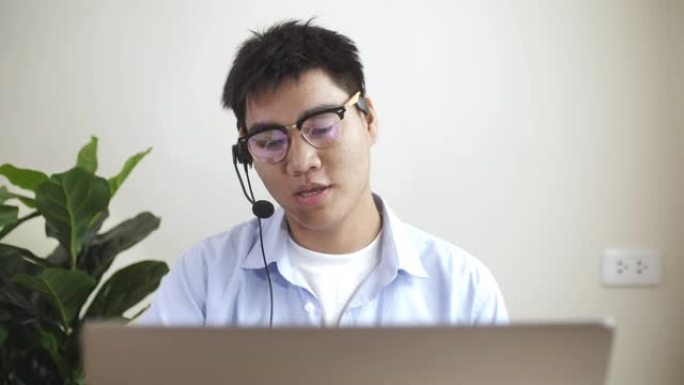 穿着蓝色休闲衬衫的亚洲男子在家里的笔记本电脑上进行视频会议，在家工作和远程工作