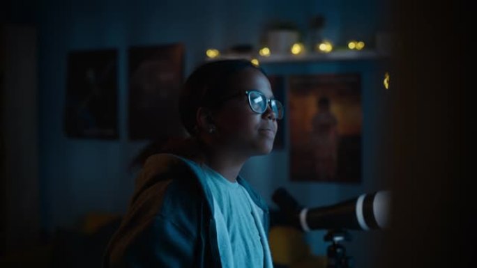 一个十几岁的多民族黑人女孩兴奋地看着窗外的肖像。惊讶的年轻女性在家里看着夜空。她戴着眼镜和牙套。