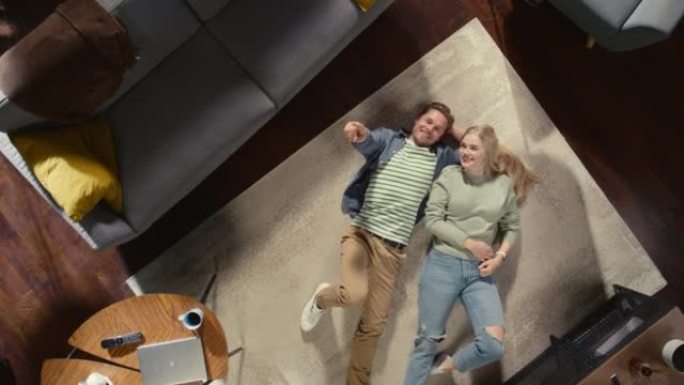 顶景公寓: 恋爱中的年轻夫妇躺在地板上聊天，分享他们的梦想，抱负和希望。女朋友和男朋友在舒适的客厅里
