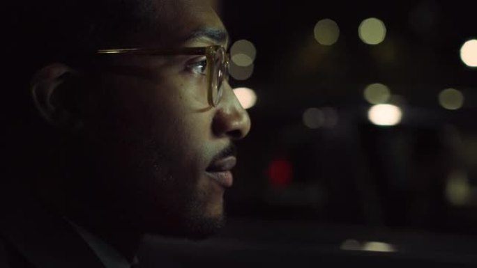 一个穿着西装的英俊黑人男子晚上开着一辆豪华轿车，专注于红绿灯。成功的非洲裔美国商人安全开车下班，思考
