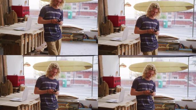 白人男性冲浪板制造商站在他的工作室里，使用他的智能手机