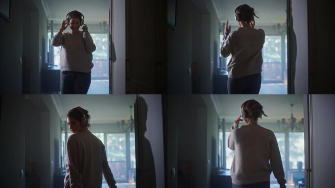 戴着耳机的快乐美女在公寓走廊里跳舞。开朗的地道女孩在家听音乐，心情愉快地跳舞。中等慢动作镜头
