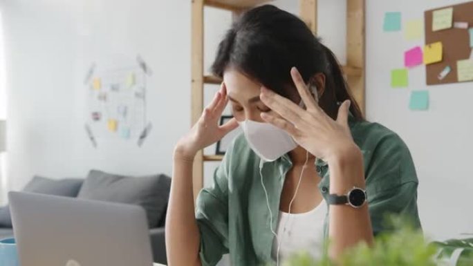 亚洲女商人在客厅在家工作时，使用笔记本电脑戴着医用口罩与同事谈论视频通话计划。