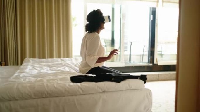 使用VR眼镜坐在酒店房间床上的非洲裔美国妇女