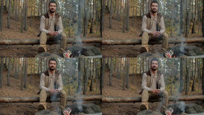 男性游客的肖像坐在树林里的火旁，拿着烤棉花糖微笑